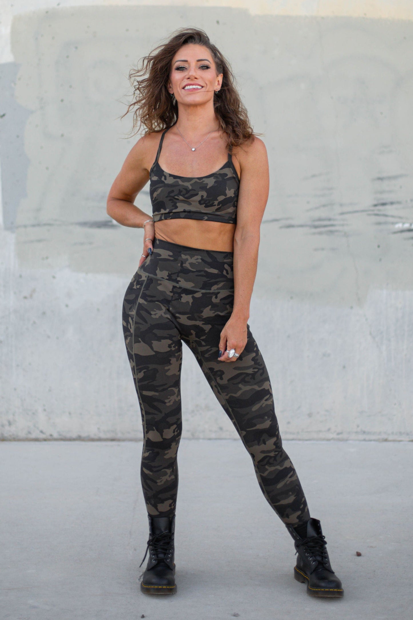 Woman in camouflage athletic wear standing against a concrete wall.