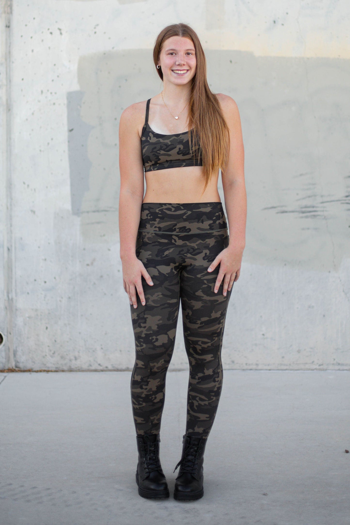 Person wearing camouflage athletic wear standing against a concrete wall.