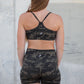 Person wearing camouflage sports bra and shorts standing against a concrete wall.