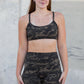 Woman wearing camouflage sports bra and shorts standing against a concrete wall.