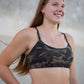 Woman wearing a camouflage sports bra and leggings against a neutral background