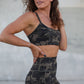 Woman wearing a camouflage sports bra and shorts set against a concrete wall.