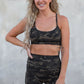 Woman wearing a camouflage sports bra and shorts set standing against a concrete wall.