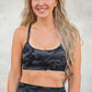 Woman wearing a black camouflage sports bra and leggings against a textured wall.