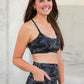 Woman wearing a black camouflage sports bra and leggings against a concrete wall.