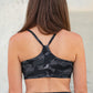 Person wearing a black camouflage sports bra and leggings against a textured wall.