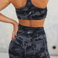 Person wearing a black camouflage sports bra and shorts set against a neutral background