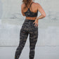 Person wearing camouflage athletic wear standing against a concrete wall.