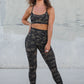 Woman in camouflage athletic wear standing against a concrete wall.