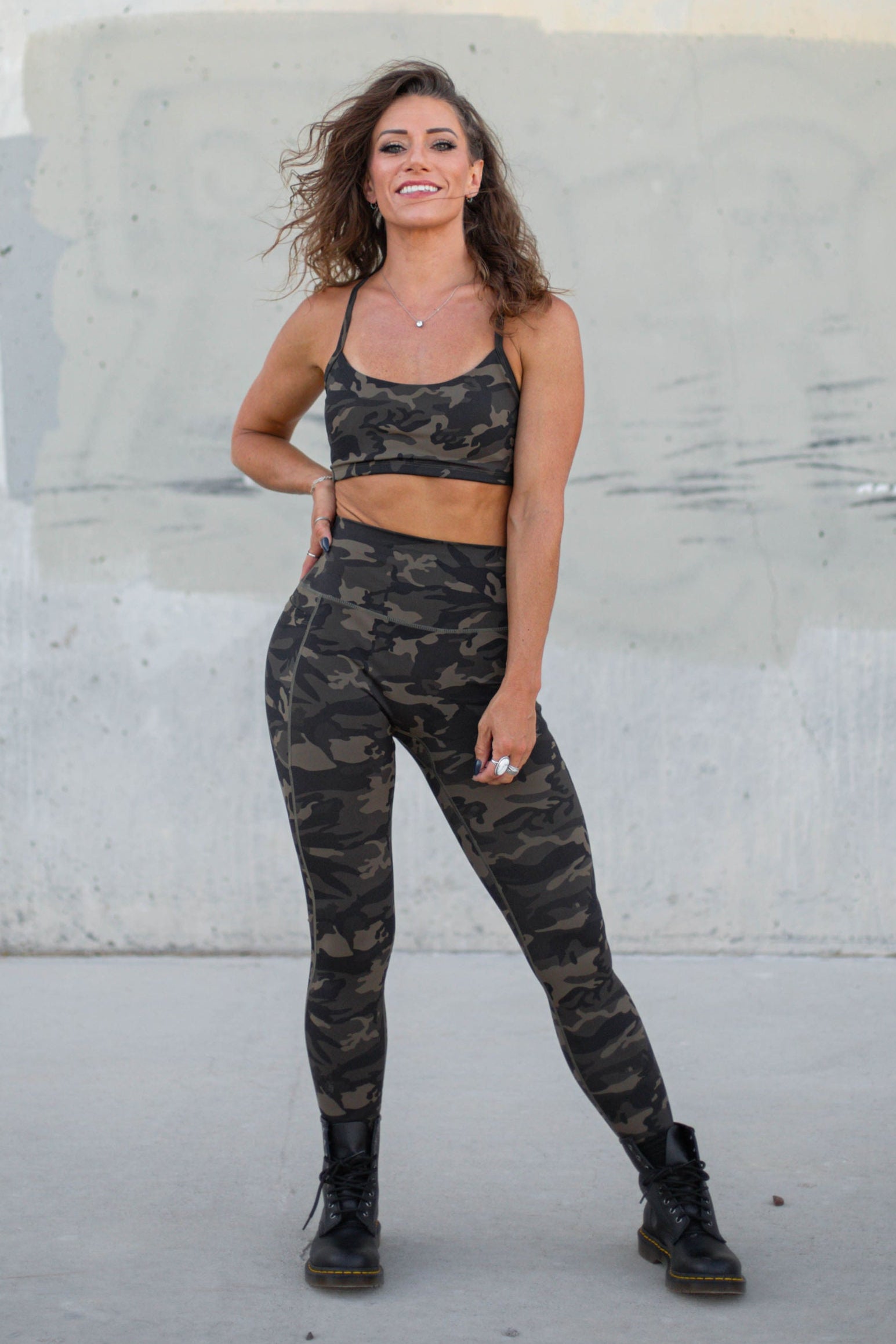 Woman in camouflage athletic wear standing against a concrete wall.