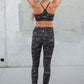 Person wearing camouflage athletic leggings and sports bra against a concrete wall.